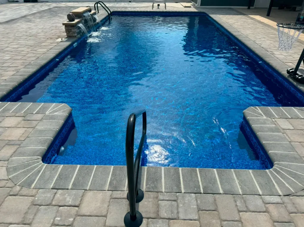 Rectangular in-ground pool with a handrail and a paver deck