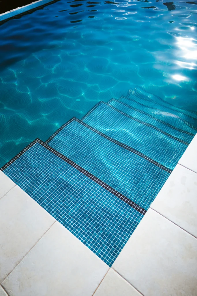 Pool steps edged in blue mosaic tile beside a light stone deck